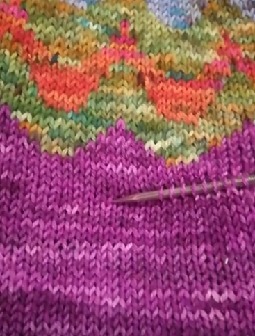 A knitting needle inserted into stitches on the body of a colourwork sweater